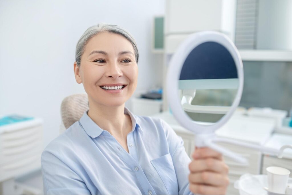 Woman sitting at the dentist's office looking at new smile in mirror