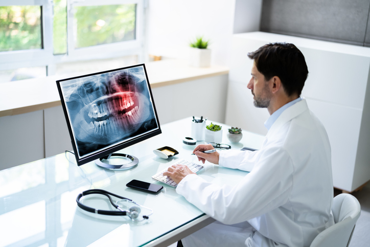 Dr. Sits at a Santa Monica Oral Surgery Center desk examining an x-ray of wisdom teeth.